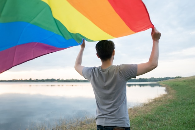 A young white man sees from behind holding a rainbow flag 