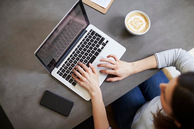 Young white woman using laptop at coffee shop overhead view