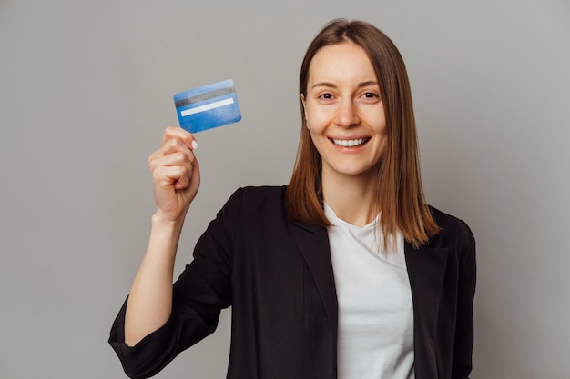 Young wide smiling woman recommends the blue credit card she is holding