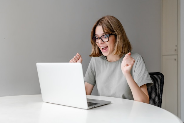 Giovane donna caucasica vincente che taring al computer portatile nell'appartamento