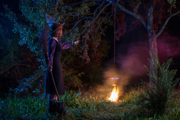 Young witch by  fire in night forest