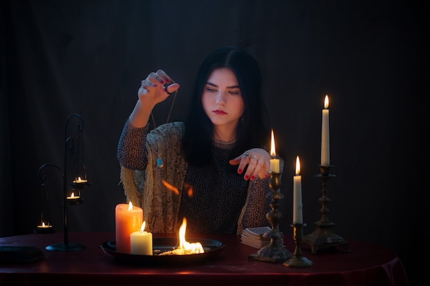 Молодая ведьма с огнем и горящими свечами на темной поверхности