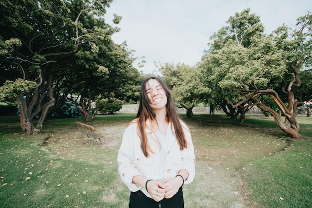 Young with long hair happy girl smiling with big teeth to\
camera in a park during a relaxing day young people smiling\
attitude towards life freedom liberty and social life concept