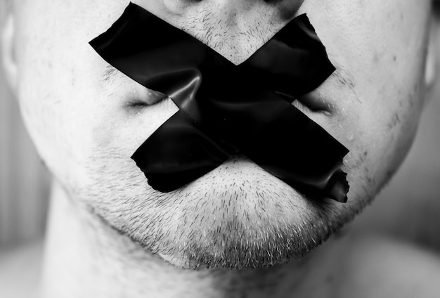 Young with scotch tape glued on his lips colorless Mouth closed with scotch tape Lips sealed with adhesive tape The concept of threats silence hiding the truth