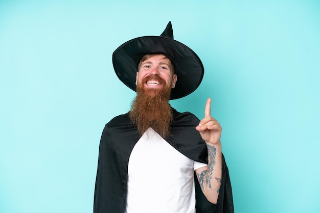 Young wizard in halloween isolated on blue background pointing up a great idea