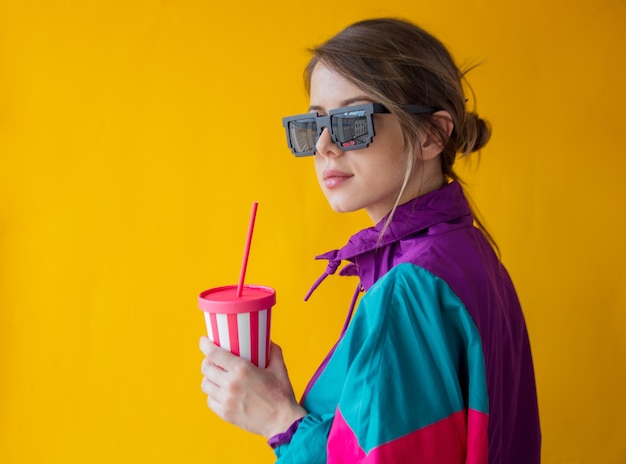 Young woman in 90s style clothes with cup on yellow