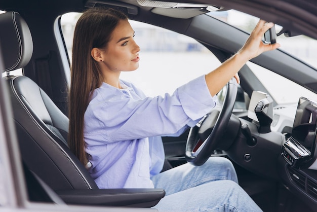 現代 車 を 運転 し て 後視 鏡 を 調整 し て いる 若い 女性