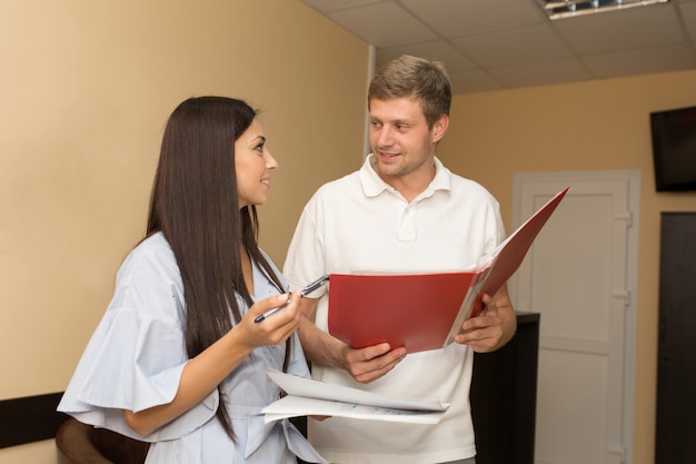 young woman administrator on reception with man looking in folder with papers