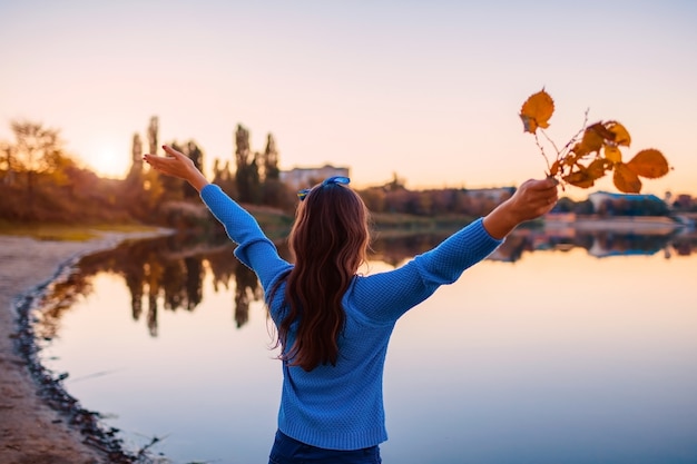 Photo young woman admiring autumn river with raised hands holding branches