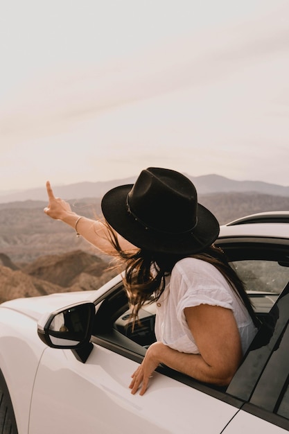 Foto giovane donna che ammira uno splendido paesaggio desertico dalla sua auto al tramonto