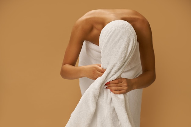 Photo young woman after shower wipes her hair with a white towel while standing