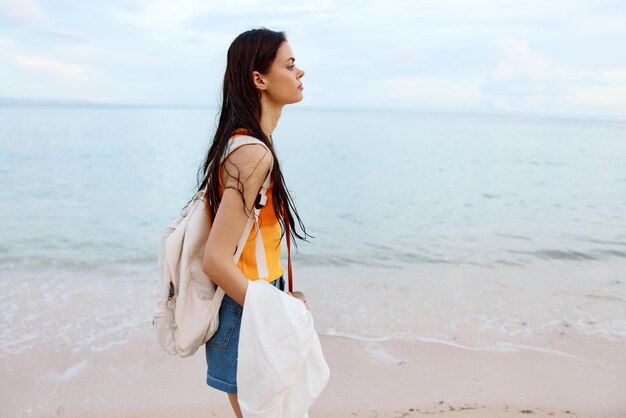 A young woman after swimming in the ocean with a backpack in wet clothes walks along the beach summer vacation on an island by the ocean in bali sunset