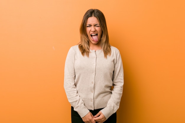 Young woman against a wall funny and friendly sticking out tongue.