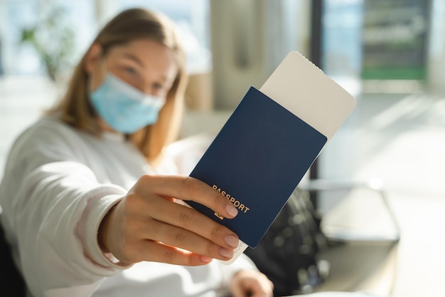 Young woman in an airport lounge during pandemic and shows her passport and ticket