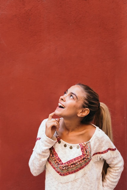 Young woman alone against a red wall looking up.