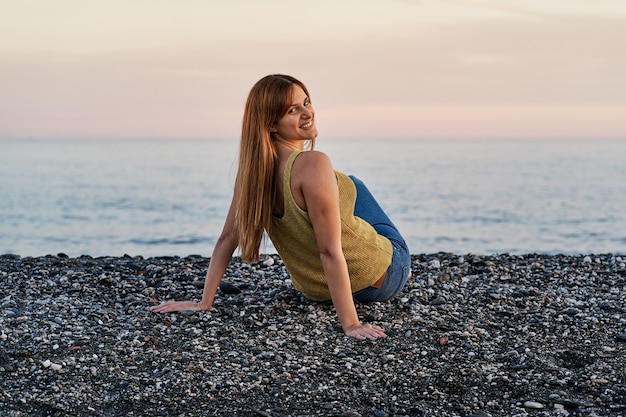 Giovane donna seduta da sola sulla spiaggia di sabbia al tramonto. concetto di rilassamento e meditazione