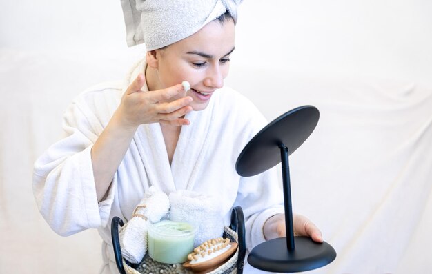 A young woman applies cream on her face looks in the mirror