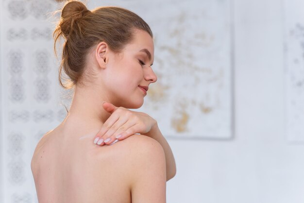 Photo young woman applying body cream at home