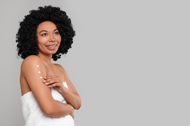 Young woman applying body cream onto arm on grey background Space for text