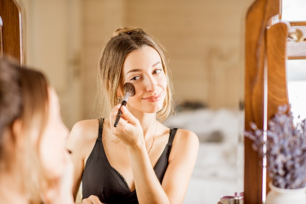 Photo young woman applying cosmetics with a brush sitting at the dressing table