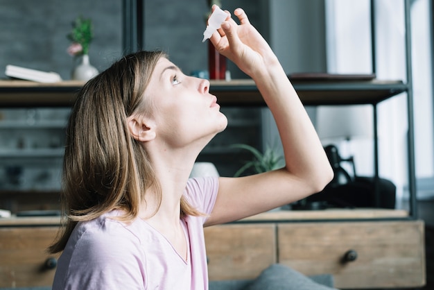 Photo young woman applying eye drops at home