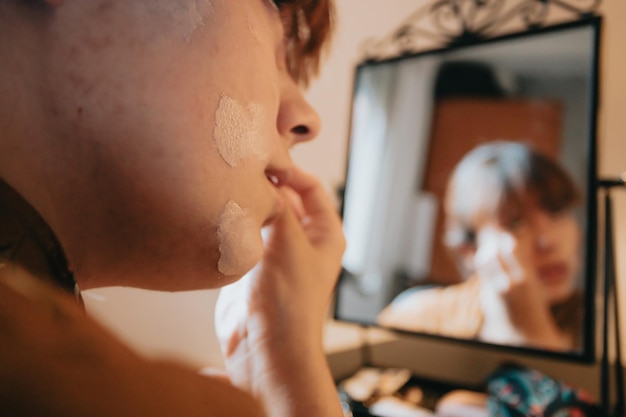 写真 リキッドファンデーションを塗っている若い女性が自宅でメイクアップベースを準備して美容。鏡を見て、黒いアイライナーで目をペイントします。閉じる