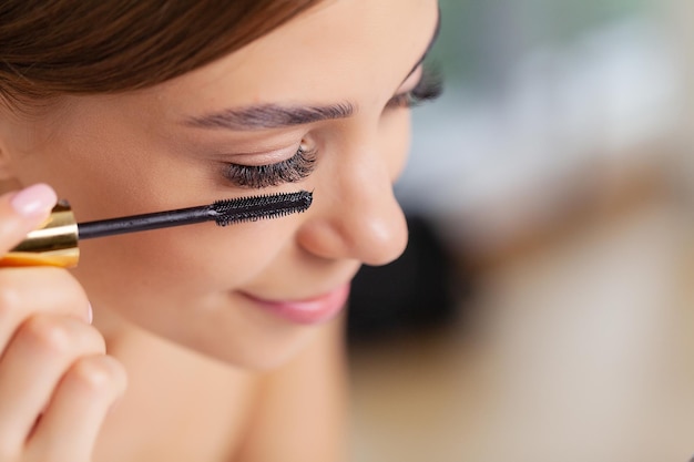 Young woman applying makeup on face at home