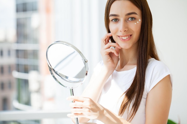 Young woman applying makeup on face at home