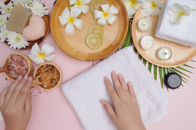 Young woman applying natural scrub on hands against white surface. Spa treatment and product for female hand spa, massage, perfumed flowers water and candles, Relaxation. Flat lay. top view.