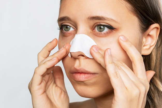 A young woman applying nose strips cleaning the skin of her
face from blackheads or black dots