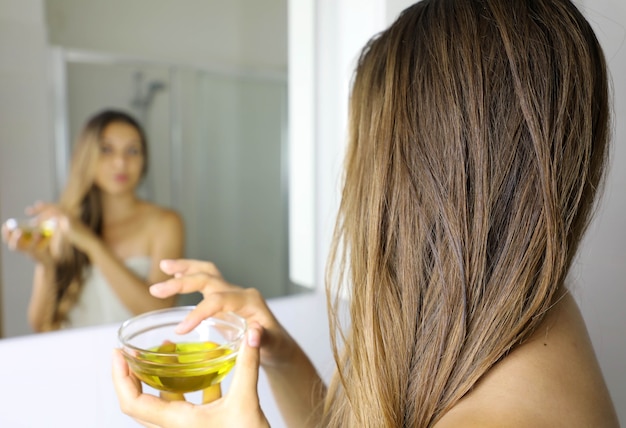 Young woman applying an olive oil mask on hair in front of a mirror |  Premium Photo