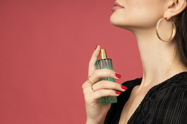 Young woman applying perfume on pink background space for text