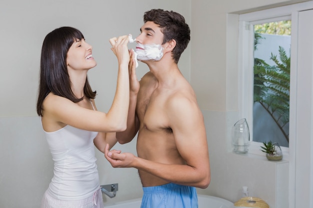 Young woman applying shaving cream on young mans face in the bathroom