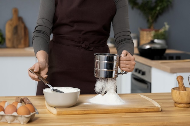 Young woman in apron sieving flour over wooden board