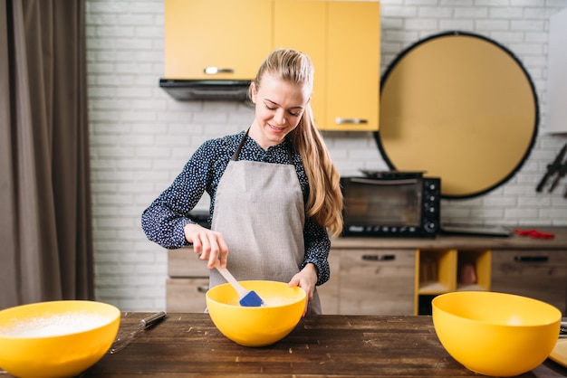 Photo young woman in apron stir the dough in a bowl on wooden table. sweet cake cooking preparation