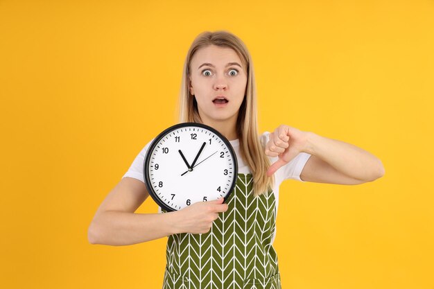 Young woman in apron with clock on yellow background