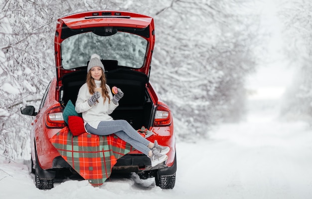 Photo young woman are sitting in a car in the winter forest and drink coffee