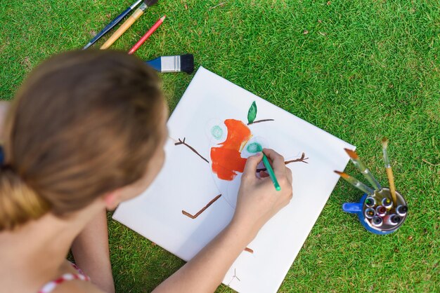 Young woman artist and illustrator drawing witha pencil laying on a lawn in summer