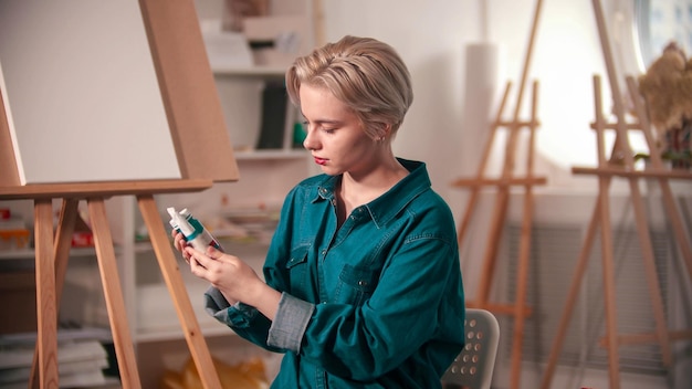 Молодая художница смотрит на два тюбика синей краски