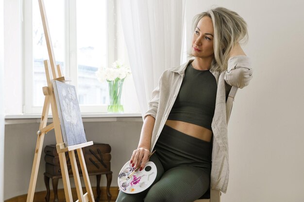 Young woman artist painting on canvas on the easel at home studio