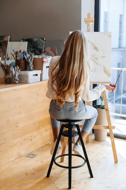 Photo young woman artist painting at home creative painting back view