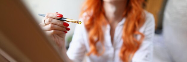 A young woman artist sits at home in front of an easel with a brush in her hand woman learning