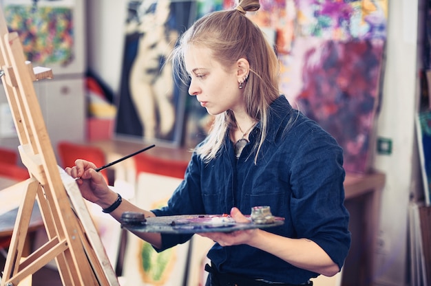 Художник молодой женщины работая на картине в студии.