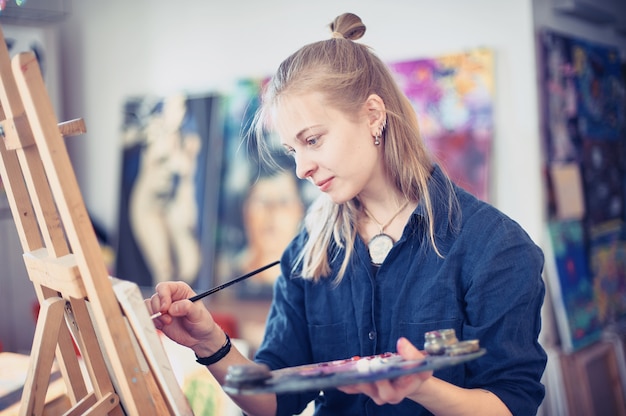 young woman artist working on painting in studio.