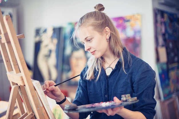 Young Woman Artist Working On Painting In Studio.