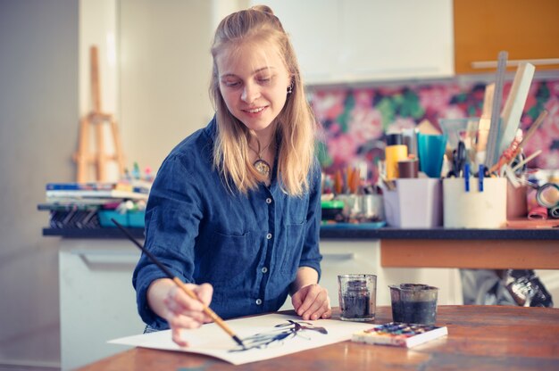 young woman artist working on painting in studio.