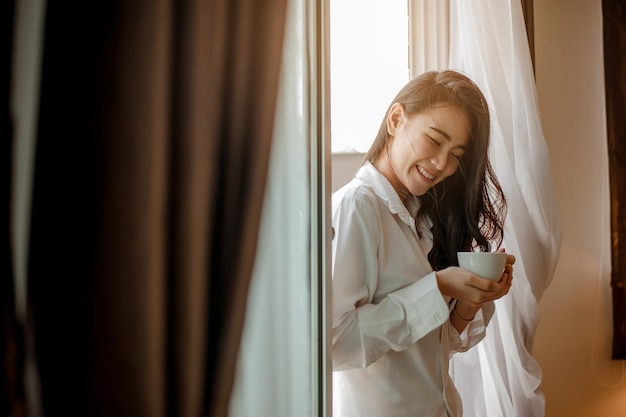 Young woman asia living at home relaxing and drinking cup of hot coffee in the bedroom on holiday. Asian, asia, relax, alone, technology, lifestyle concept.