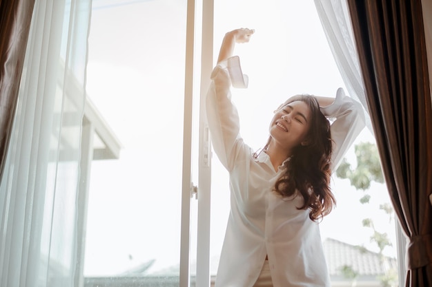 若い女性アジアは朝にさわやかに目を覚まし、休日に寝室でリラックスします。アジア、アジア、リラックス、一人で、テクノロジー、ライフスタイルのコンセプト。