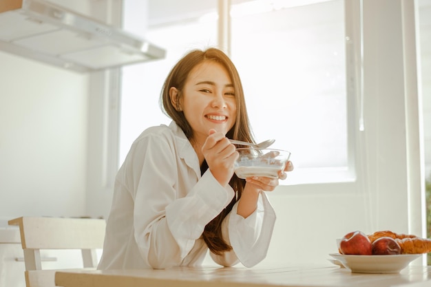 Young woman asia wake up refreshed in the morning and relaxing\
eat coffee, cornflakes, bread and apple for breakfast at house on\
holiday. asian, asia, relax, breakfast, refresh, lifestyle\
concept.