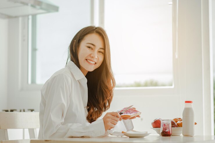 Photo 若い女性アジアは朝にさわやかに目を覚まし、休日の家で朝食にコーヒー、コーンフレーク、パン、リンゴを食べてリラックスします。アジア、アジア、リラックス、朝食、リフレッシュ、ライフスタイルのコンセプト。